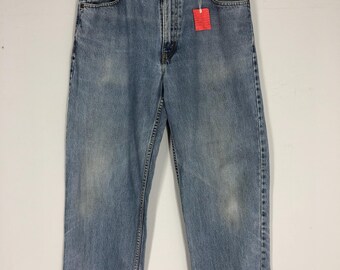 May include: Light blue denim jeans with a relaxed fit, hanging on a wooden hanger. The jeans have a faded appearance and a red tag attached. The jeans are a classic style.