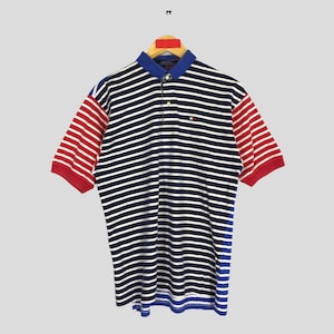 May include: A striped navy blue and white polo shirt with red and blue striped sleeves. The shirt has a small embroidered logo on the left chest.