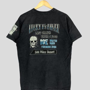 May include: Black t-shirt featuring a skull graphic and the text "Lucky P's Diner" with the words "Last Chance", "Water & Food", "Ice Water Bags", "Thermos Jugs", and "500 Miles Desert".
