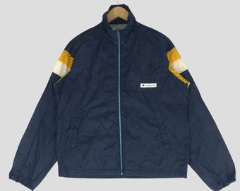May include: A navy blue windbreaker jacket with a zipper closure and a white and yellow stripe detail on the sleeves. The jacket has a Champion logo patch on the left chest.