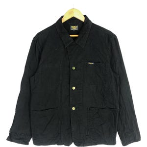 May include: A black workwear jacket with a button-up front, two chest pockets, and two lower pockets. The jacket has a yellow label with the text "Denime" on the left chest.