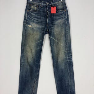 May include: A pair of blue denim jeans with distressed details and a red tag hanging from the waistband.