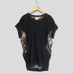 Puede incluir: Una camiseta gris oscura de manga corta con estampado floral en los laterales. La camiseta tiene un cuello redondo y un corte holgado.