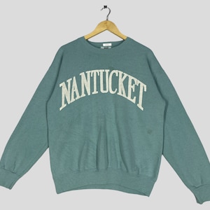 Puede incluir: Una sudadera azul verdosa con la palabra "NANTUCKET" impresa en blanco en la parte delantera.