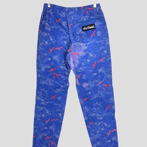 May include: Blue pants with a white and red bird pattern. The pants have a zippered pocket on the back right side and a black label that says "Wild Things" on the back right side.