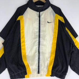 May include: A black and white windbreaker jacket with yellow accents. The jacket has a zipper closure and a Nike logo on the right chest.