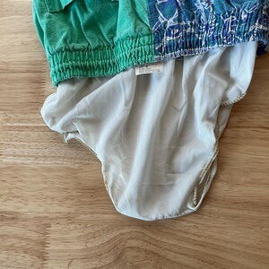 May include: A green and blue patterned garment with a white lining. The top portion is green with a ribbed waistband, while the bottom is a light blue with a white pattern. The lining is a light beige color.