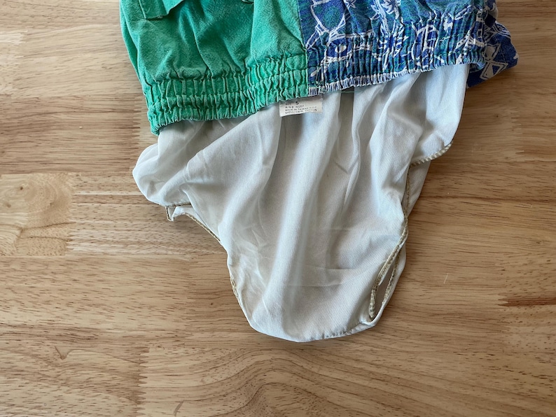 May include: A green and blue patterned garment with a white lining. The top portion is green with a ribbed waistband, while the bottom is a light blue with a white pattern. The lining is a light beige color.