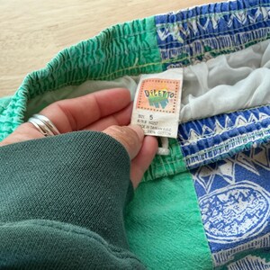 May include: Vintage children's shorts with a colorful design. The shorts feature a green waistband and a blue and white patterned lower section. The tag reads "DILETTO" and "SIZE 5". Made of 100% cotton.
