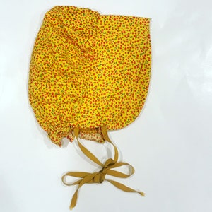 May include: A yellow fabric bonnet with a red floral pattern and a brown ribbon tie.