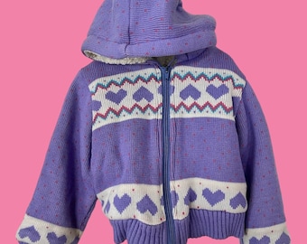 May include: A purple knitted zip-up jacket with a white and pink heart pattern. The jacket has a hood and a zipper closure.