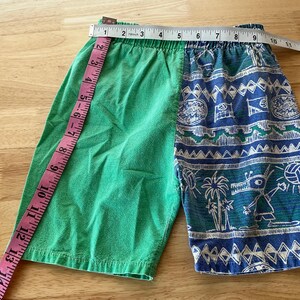 May include: Green and blue patterned shorts with a measuring tape. The shorts are divided into two sections: solid green and a blue pattern with white accents. The shorts measure approximately 14 inches across the waist.