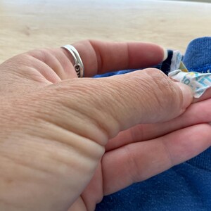 May include: Close-up of a blue t-shirt with a white tag attached to the collar. The tag has the words "100% Cotton" printed on it.