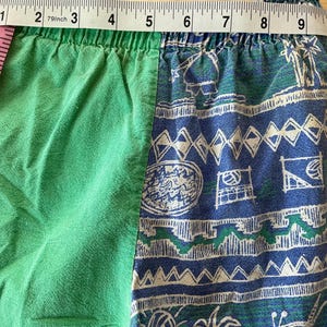May include: Green and blue patterned shorts. The shorts have a green solid color on the left side and a blue and white patterned design on the right side. The waist measures approximately 8 inches (20 cm) across.