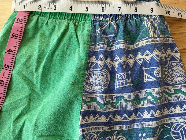 May include: Green and blue patterned shorts. The shorts have a green solid color on the left side and a blue and white patterned design on the right side. The waist measures approximately 8 inches (20 cm) across.