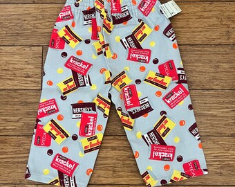 May include: Gray pants with a pattern of Hershey's chocolate bars, including Krackel, Mr. Goodbar, and Special Dark. The pattern also includes red and yellow candy-like shapes.