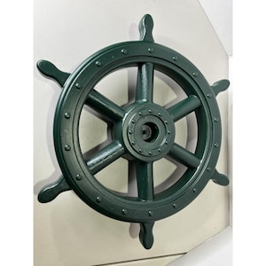 May include: A dark green ship's wheel with six spokes and four handles. The wheel is made of a solid material and has a circular design with rivets around the outer edge. The nautical decor piece is mounted on a light-coloured wall.