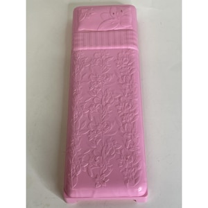 May include: A rectangular pink plastic toy bed featuring a molded pillow with a floral design at the head. The surface of the bed is decorated with an embossed pattern of climbing flowers and leaves that extends across the entire length of the frame.