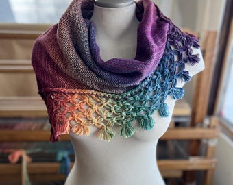 May include: A rainbow ombre scarf with a crocheted fringe. The scarf is made of a soft, textured yarn and has a gradient of colors from purple to green.