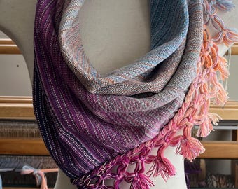May include: A gradient-colored woven scarf with a fringe border. The scarf is displayed on a white mannequin and features a blue, pink, and purple color scheme.