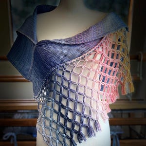 May include: A multi-coloured shawl on a mannequin. The shawl has a woven design, with a gradient from blue to pink and yellow. The bottom edge of the shawl is finished with a fringe. The shawl is handmade.