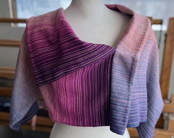 May include: A purple, pink, and blue striped woven shawl with a gradient effect. The shawl is draped over a white mannequin.