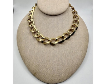 May include: A gold-toned chain necklace with large, interlocking links. The necklace is displayed on a beige bust, showcasing its bold design and substantial presence. The chain's color is a bright, polished gold.