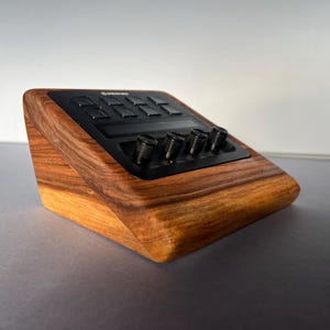 以下が含まれることがあります： ボタンとノブを備えた黒いコントロールパネルを備えた木製の電子デバイス。デバイスは、豊かで温かみのある木目仕上げと洗練されたモダンなデザインです。コントロールは黒です。