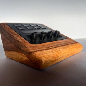 以下が含まれることがあります： 黒いコントロールパネルを備えた木製の電子機器。デバイスは濃い木目仕上げで、いくつかの黒いノブとボタンを備えています。デザインは角度があり、機能性と美しさに焦点を当てたモダンなデザインです。