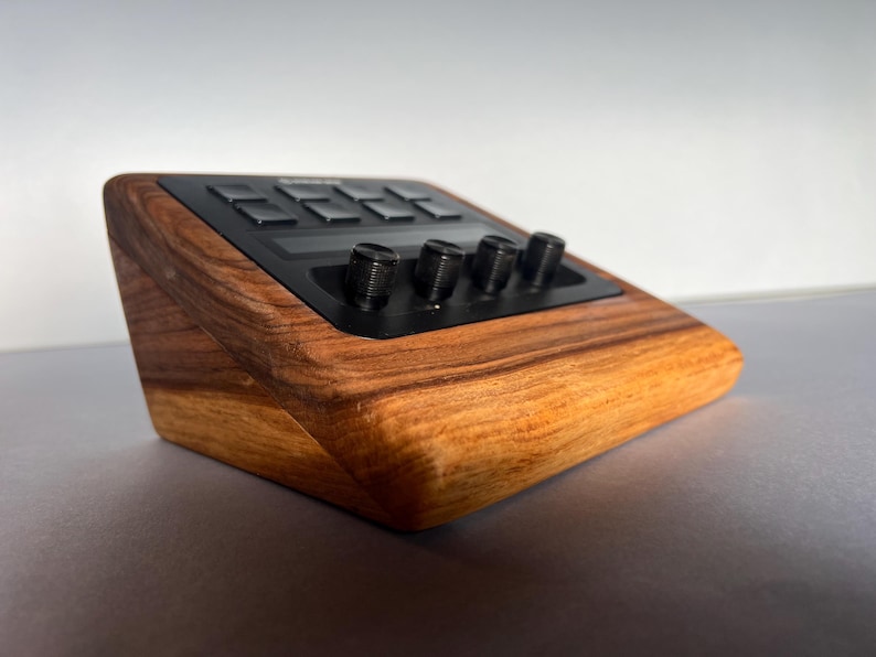 以下が含まれることがあります： 黒いコントロールパネルを備えた木製の電子機器。デバイスは濃い木目仕上げで、いくつかの黒いノブとボタンを備えています。デザインは角度があり、機能性と美しさに焦点を当てたモダンなデザインです。