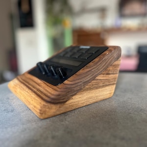 以下が含まれることがあります： 黒いコントロールパネルを備えた木製の電子機器スタンド。スタンドは明るい茶色と濃い茶色の木材でできており、傾斜したデザインです。コントロールパネルにはボタンとノブがあります。