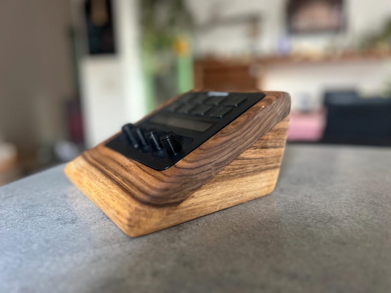 以下が含まれることがあります： 黒いコントロールパネルを備えた木製の電子機器スタンド。スタンドは明るい茶色と濃い茶色の木材でできており、傾斜したデザインです。コントロールパネルにはボタンとノブがあります。