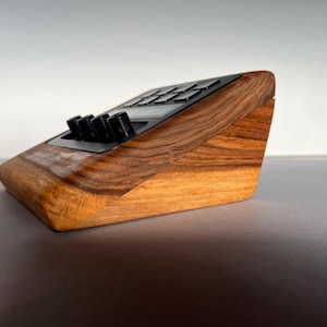 以下が含まれることがあります： 木製の角度付きオーディオインターフェース。濃い木目調の仕上げ。黒いノブとボタンが黒いパネルに配置されています。ベースは明るい木の色合いで、暗い上部とのコントラストを生み出しています。