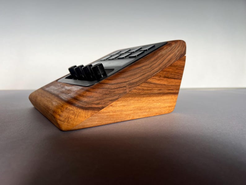 以下が含まれることがあります： 木製の角度付きオーディオインターフェース。濃い木目調の仕上げ。黒いノブとボタンが黒いパネルに配置されています。ベースは明るい木の色合いで、暗い上部とのコントラストを生み出しています。