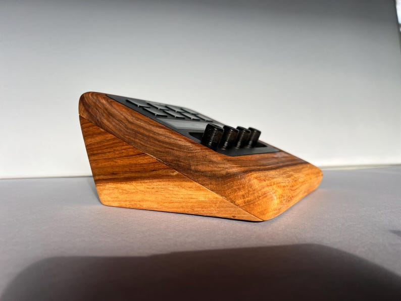 以下が含まれることがあります： ボタンとノブを備えた黒いトップを備えた木製の電子デバイス。デバイスは、明るい茶色と濃い茶色の木材でできており、傾斜したデザインになっています。ノブは黒く、円筒形です。