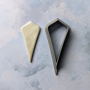 May include: A set of two cookie cutters, one is a silver-colored diamond shape and the other is a white diamond shape.