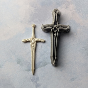 May include: Two swords, one silver and one gray, are displayed against a light blue background. The silver sword is smaller and has a more intricate design. The gray sword is larger and has a simpler design.