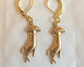 May include: A pair of gold-tone earrings featuring a hand design with a raised, textured surface. The earrings have a hook closure.