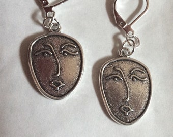 May include: A pair of silver earrings with a face design. The earrings are made of metal and have a hook closure.