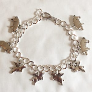 Pulsera Pigs Might Fly Pigs with Wings dije en tono plateado longitudes disponibles de 19 a 21 cm y pendientes a juego