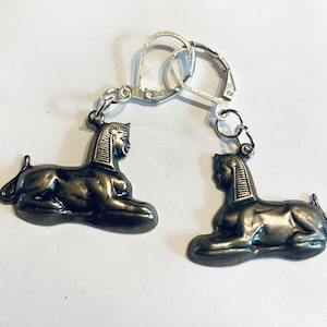 May include: A pair of silver earrings with a bronze sphinx charm on each earring.