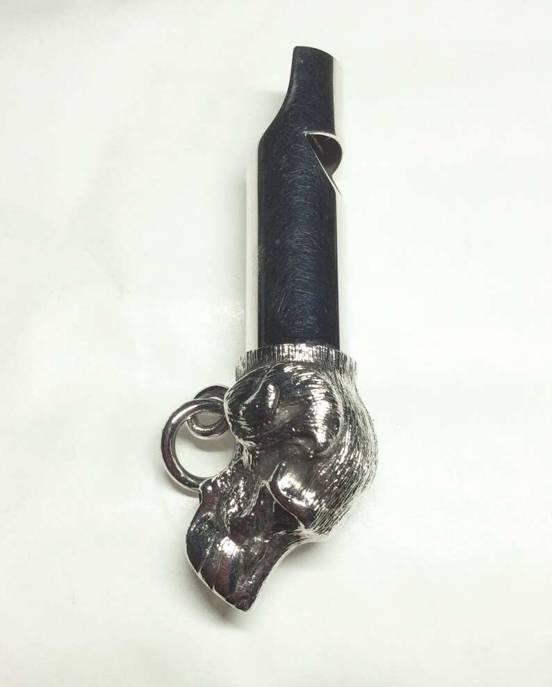 May include: Silver whistle with a detailed dog head design. The whistle has a ring for attaching to a keychain or lanyard.
