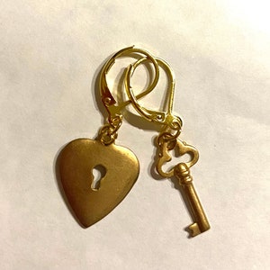 Könnte beinhalten: Goldene herzförmige Ohrringe mit einem Schlüssellochdetail und einem passenden Schlüsselanhänger.
