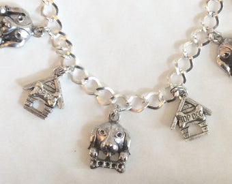 May include: Silver charm bracelet featuring dog-themed charms, including a dog house with "Top Dog" inscribed on it, and several dog figures.