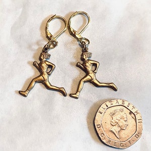 May include: Gold-toned earrings featuring a running figure design. The earrings have a leverback closure.
