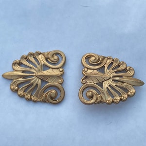 May include: Two gold-colored metal decorative pieces with a floral design. The pieces are intricate and detailed, with a fan-like shape in the center.