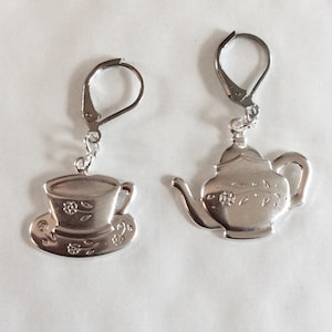 Peut inclure: Une paire de boucles d'oreilles en argent, l'une en forme de théière et l'autre en forme de tasse à thé et de soucoupe. Les deux boucles d'oreilles présentent des motifs floraux.
