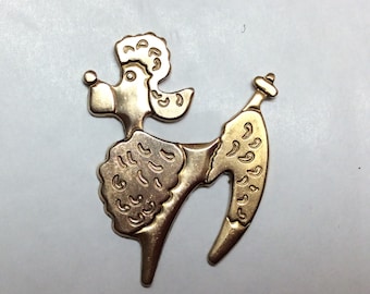 May include: Gold-toned metal brooch in the shape of a poodle with a curly tail. The poodle has a detailed design with a textured surface.