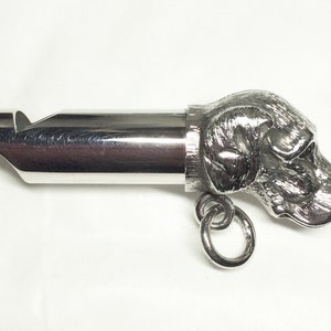 May include: Silver dog whistle with a detailed dog head design. The whistle has a ring attached for easy carrying.