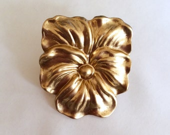 May include: A gold-toned metal flower brooch with a textured surface. The flower has five petals and a center button.